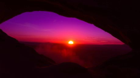 Witness the breathtaking spectacle of a desert sunset framed by a natural rock arch, painted in intense ultraviolet and purpl
