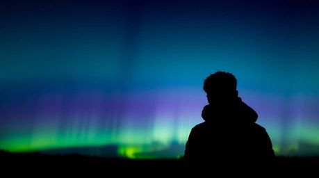 This image captures a silhouetted subject bathed in the ethereal glow of backlighting, reminiscent of the aurora borealis. A