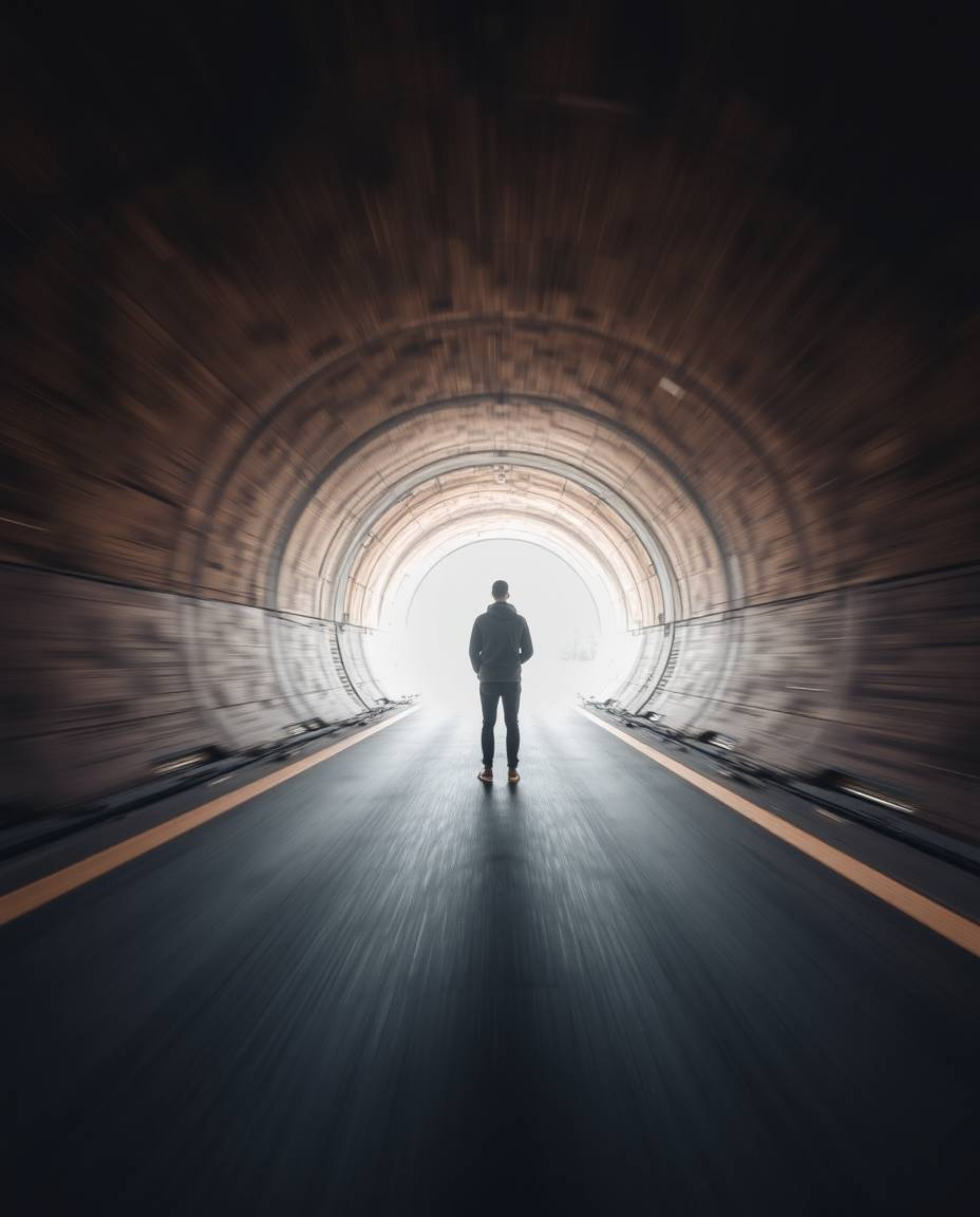A captivating long-exposure photograph showcases a person silhouetted at a tunnel's entrance, gazing towards a radiant light 