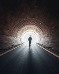 A captivating long-exposure photograph showcases a person silhouetted at a tunnel's entrance, gazing towards a radiant light 