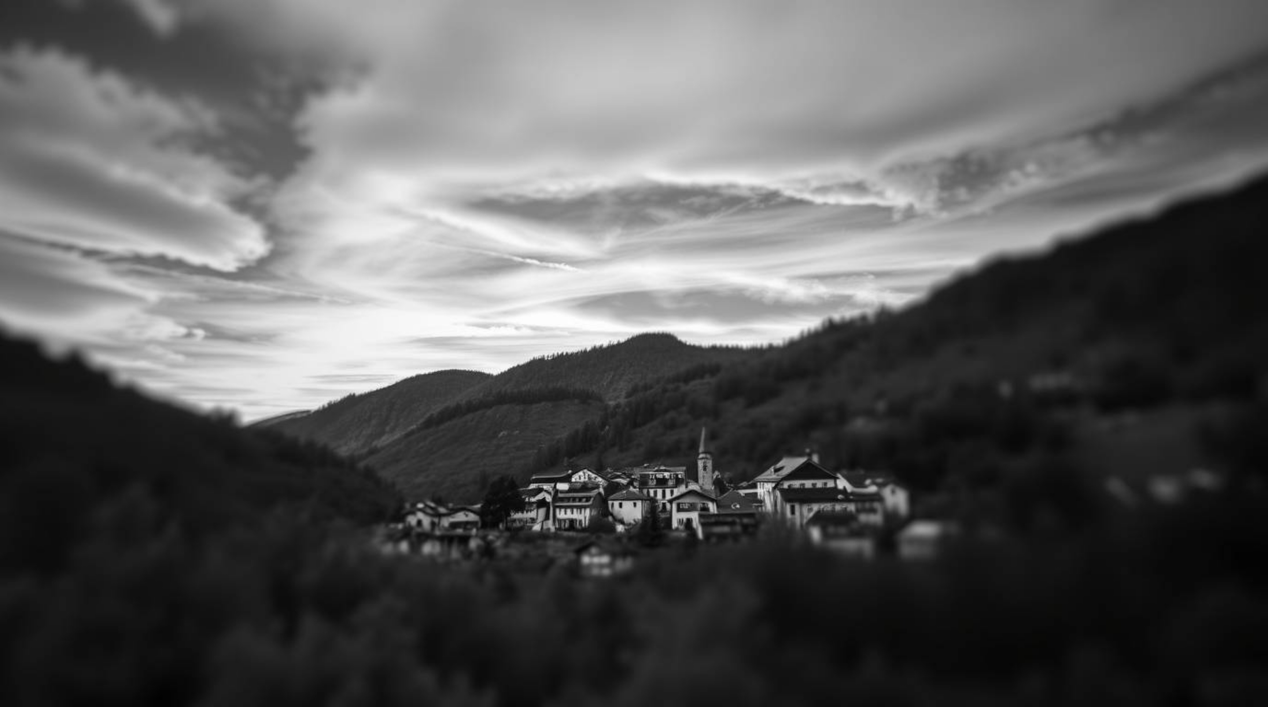 A classic black and white photograph captures a cozy village nestled in a valley beneath a vibrant, colorful sky. The sharp f