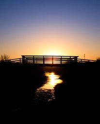 An extreme macro close-up captures the intricate details of an old wooden bridge over a river at sunset. The image is rendere