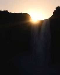 Chiaroscuro lighting emphasizes a sun setting behind a dramatic waterfall, creating strong contrasts and deep shadows. The co
