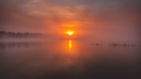 Capture the dreamy atmosphere of a serene lake reflecting a vivid sunset.  Warm autumn colors, soft light, and a hazy effect 