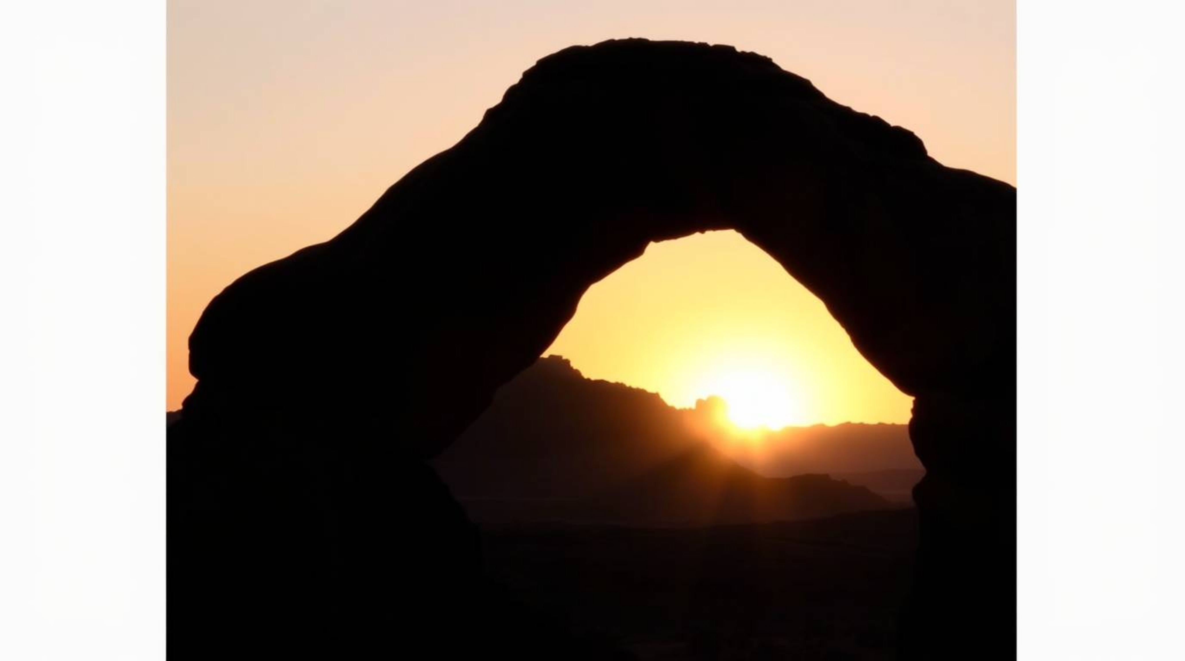 Experience the breathtaking beauty of a desert sunset framed by a natural rock arch. This image captures a backlit silhouette