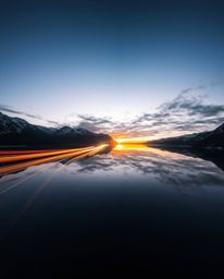 A stunning long exposure photograph capturing the beautiful motion of light trails from a sunset as they reflect in a glassy 