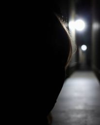 An intensely lit image showcasing eyes watching intently from the shadows of a dimly lit alley at night. The high contrast em