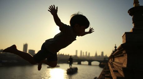 A silhouetted young boy with dark hair and fair skin is captured in a low-angle perspective, flying above London with barely 