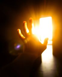 A captivating image depicts a blurred, radiant hand dynamically reaching towards a light source emerging from darkness.  The 