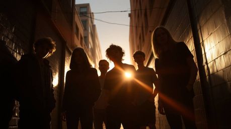 A captivating high-resolution stock photo depicts rebellious teens silhouetted against the dramatic backlighting of a grungy 