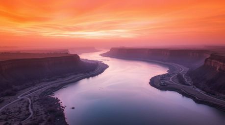 A captivating high-resolution stock photo depicting a winding river bathed in the glow of a dramatic orange-pink sunset. The 