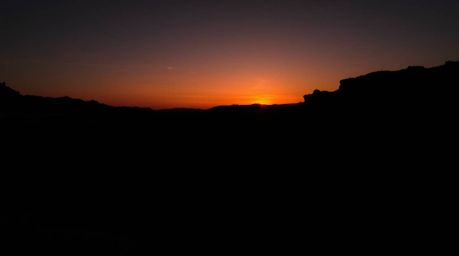 A captivating high-contrast photograph showcases a rugged rocky canyon at sunset.  Deep shadows and intense blacks dominate t