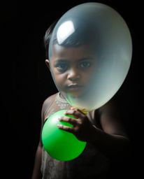 A captivating image of a child with dark skin holding a balloon, captured in a strong moody style.  Intense, dramatic lightin