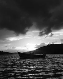 Classic black and white photograph of a boat on a lake during a dramatic sunset, intense weather and cinematic style evoke a 