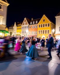 This long exposure photograph captures the vibrant energy of a musical number in a brightly lit town square. Utilizing cool c