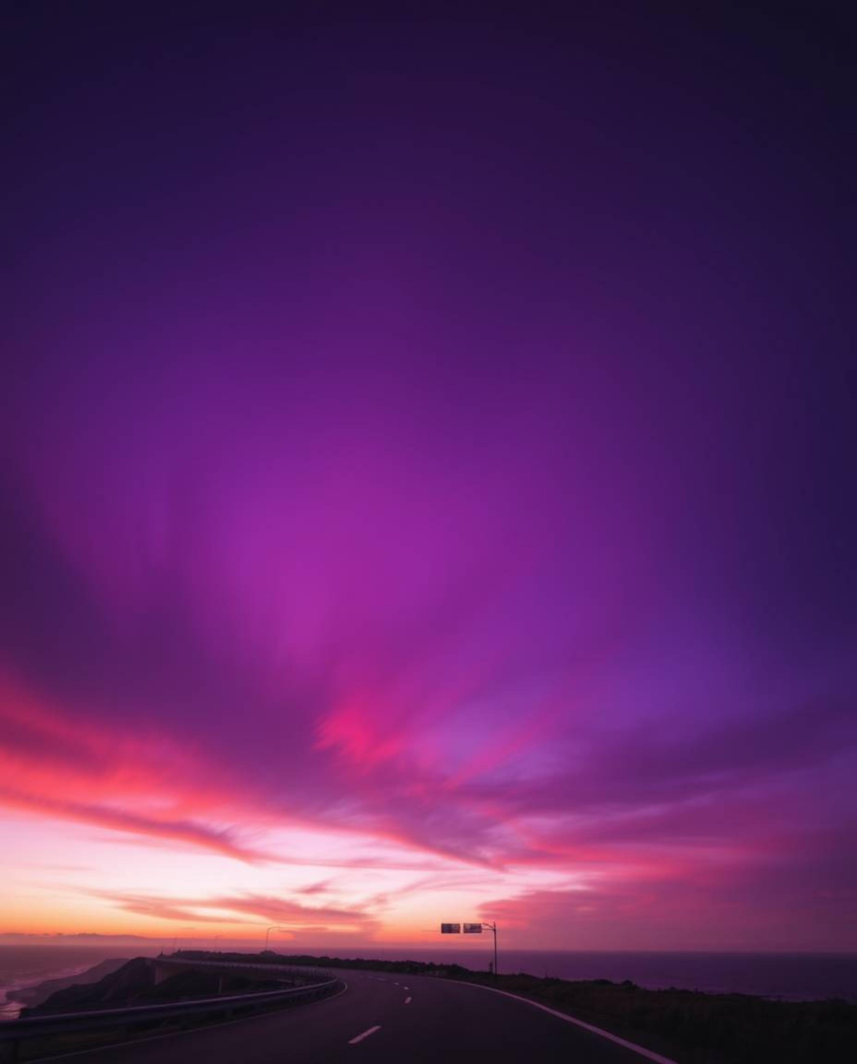 This image showcases a sunset sky over a winding coastal highway, brought to life through a dramatic palette of deep ultravio