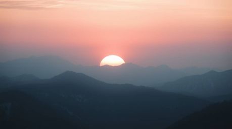 A moody depiction of snow-covered mountains bathed in the soft, pastel hues of a sunset. The scene is enhanced with a soft ci