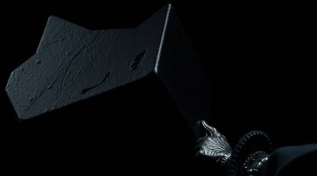 A striking, intensely detailed, jet-black close-up image showcasing an anvil poised to crush a trickster character. The pure 