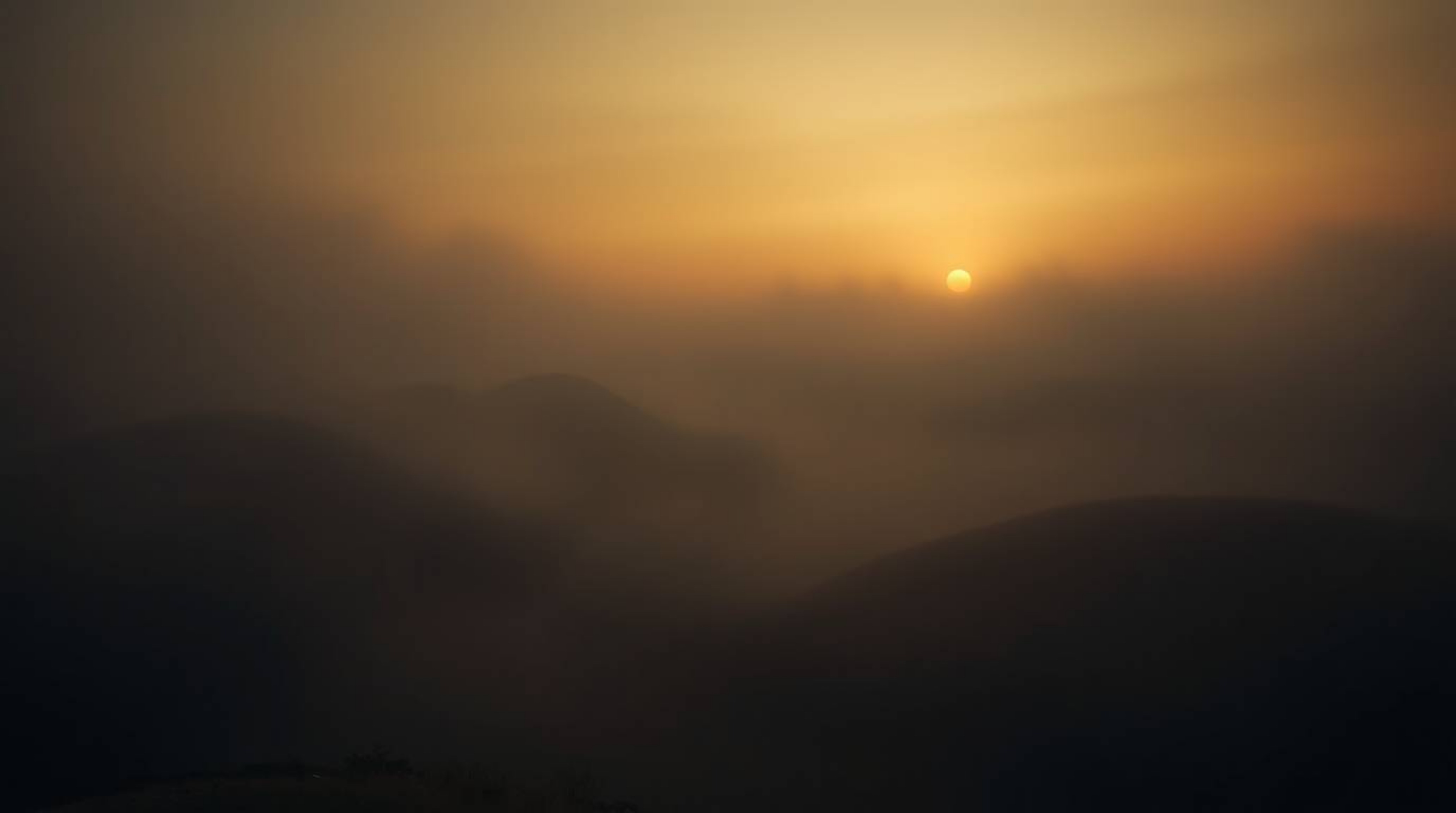 Capture the unsettling atmosphere of fog-covered hills bathed in the warm glow of a sunset. This image showcases volumetric l