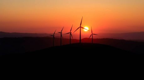 A stunning split composition photograph captures a serene sunset behind a row of wind turbines perched atop a hill.  The imag