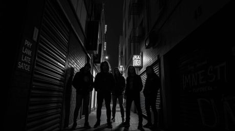 A captivating high-contrast black and white photograph depicts a grungy city alleyway teeming with rebellious teenagers.  Bio
