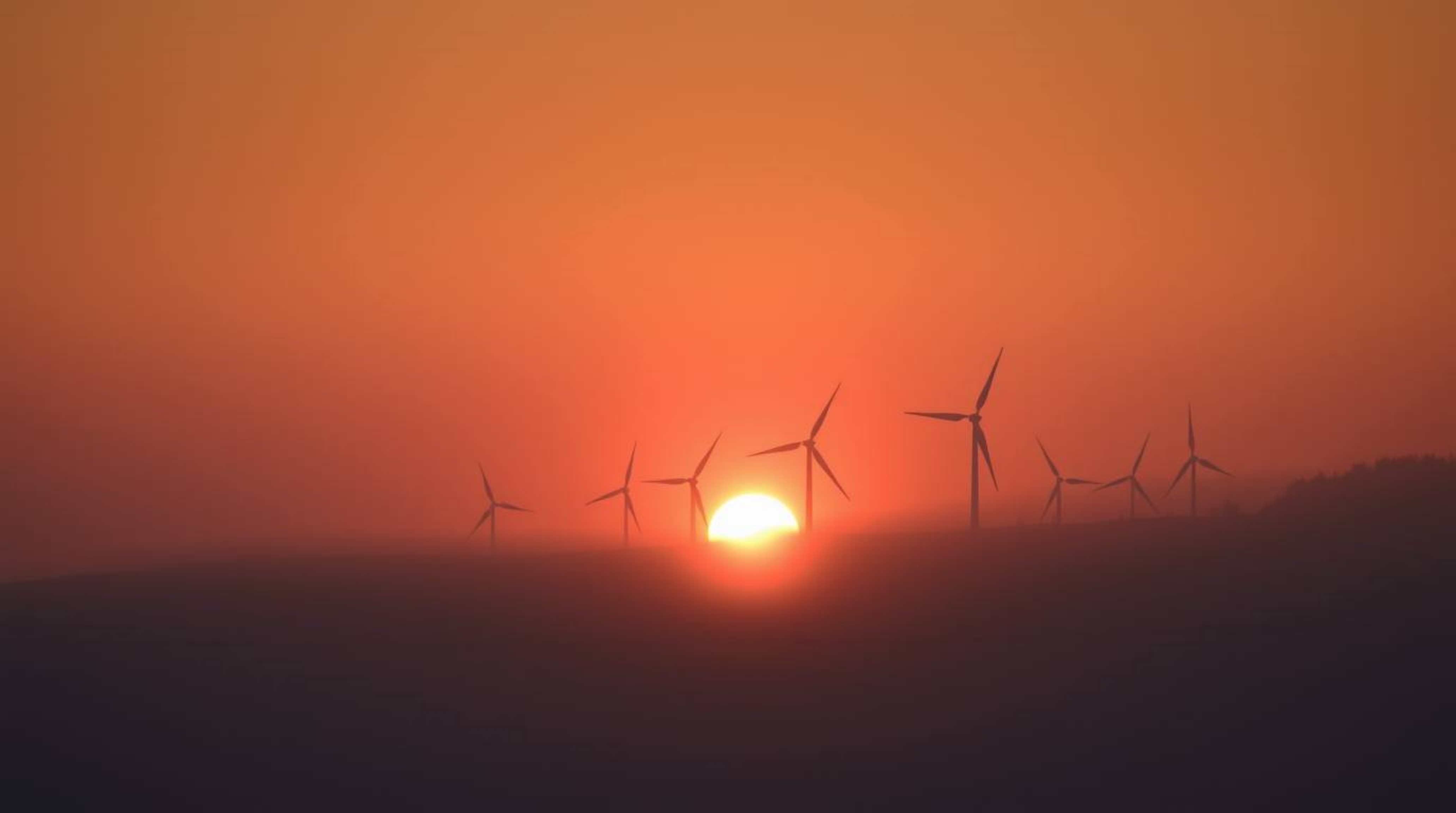 A stunning fine art photograph captures a breathtaking sunset behind a row of wind turbines perched atop a hill, shrouded in 