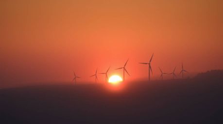 A stunning fine art photograph captures a breathtaking sunset behind a row of wind turbines perched atop a hill, shrouded in 