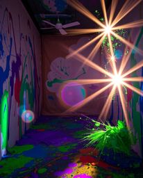 Experience the chaos and beauty of a room exploding with paint, where vibrant blues, greens, and purples dance under the illu