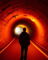 A captivating fine art photograph depicts a person standing at the edge of a tunnel, gazing towards a radiant light source.  