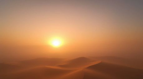Experience the breathtaking beauty of a sunset over golden desert dunes, shrouded in a thick fog. This high-angle perspective