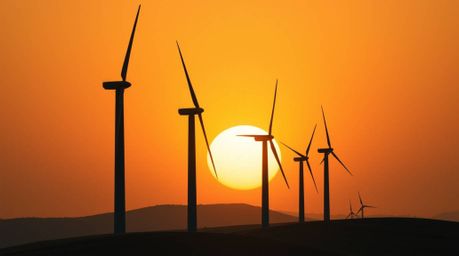 This image captures a precise architectural color photograph of a breathtaking sunset behind a row of wind turbines perched a