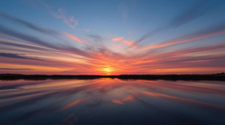 Capture the serene beauty of a colorful sunset mirrored in the tranquil waters of a calm pond. This image evokes a sense of f