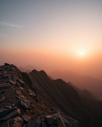This is a high-contrast photograph of a sunset as viewed from a high alpine peak. The composition showcases a palette of natu
