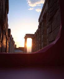 An intricate origami-style artwork depicts a sunset casting shadows through ancient stone ruins. Using bright, vibrant colors