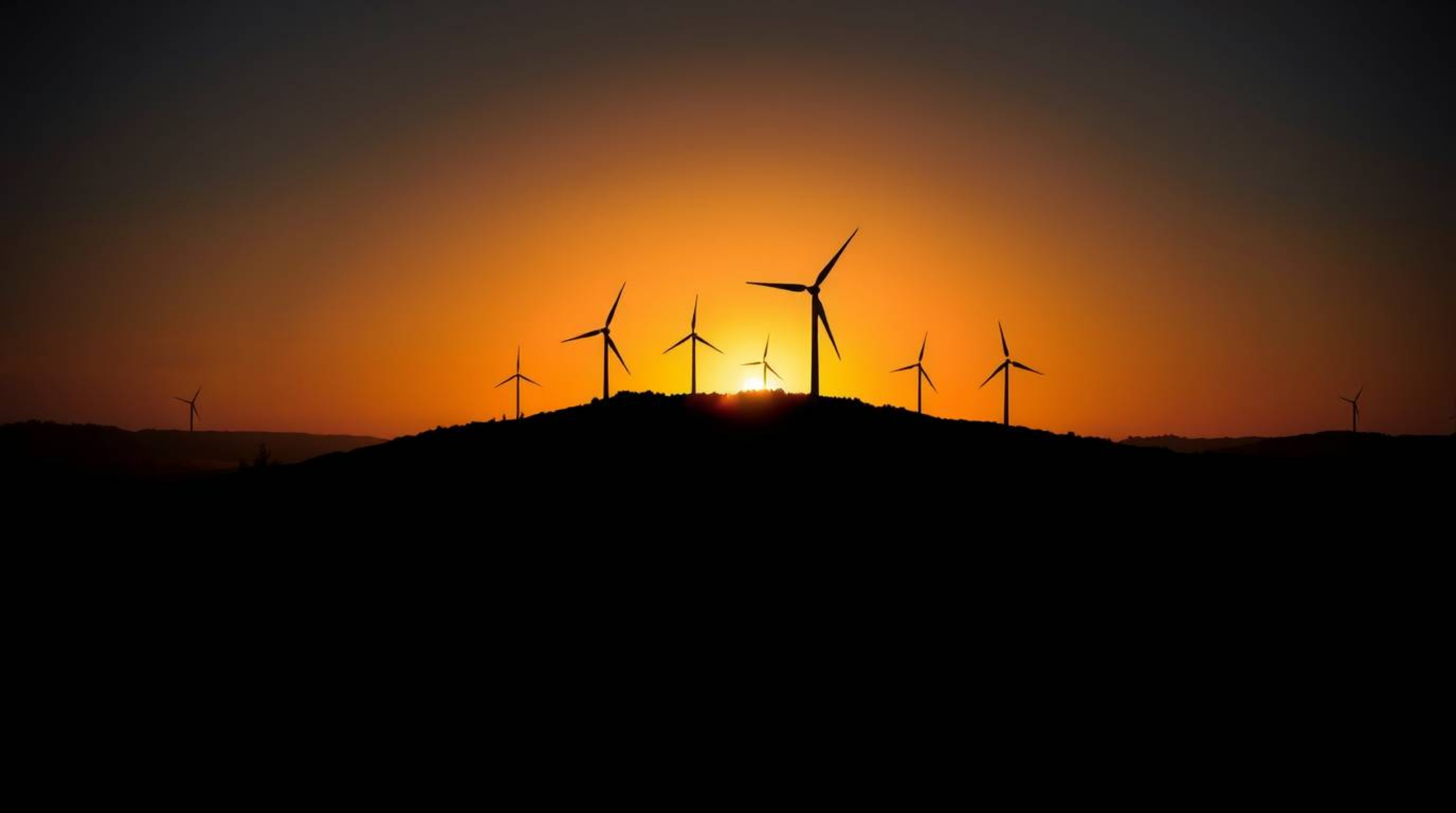 A stunning chiaroscuro image capturing a sunset behind wind turbines atop a hill. The scene is characterized by strong contra