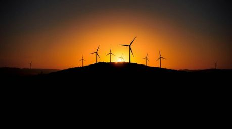 A stunning chiaroscuro image capturing a sunset behind wind turbines atop a hill. The scene is characterized by strong contra