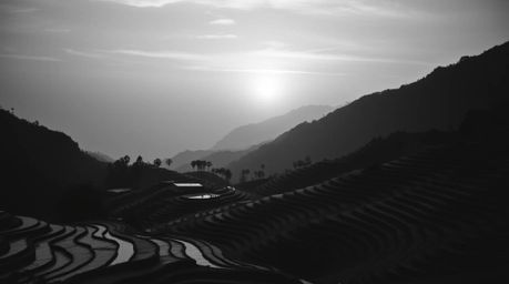 A timeless black and white photograph showcasing an elegant composition of a sunset over rice terraces in a mountainous lands