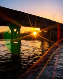 An extreme macro close-up captures the intricate details of an old wooden bridge over a river at sunset. The image is rendere