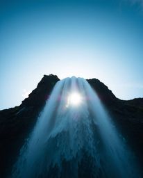 A stunning low-angle shot captures a dramatic waterfall with the sun setting behind it. This image emphasizes an upward persp