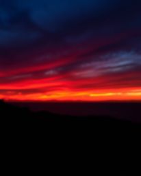 This photograph captures a sunset sky over a winding coastal highway, defined by its intense, jet-black sky and deep shadows.