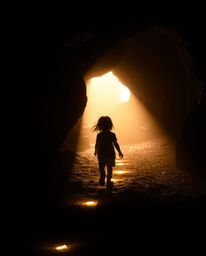 A captivating fine art photograph featuring a child with windswept hair following a trail of glowing footsteps into a cave. T