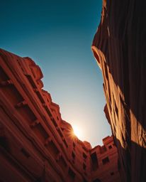 A precise architectural color photograph captures a sunset illuminating sandstone cliffs, taken from a dramatic low-angle per