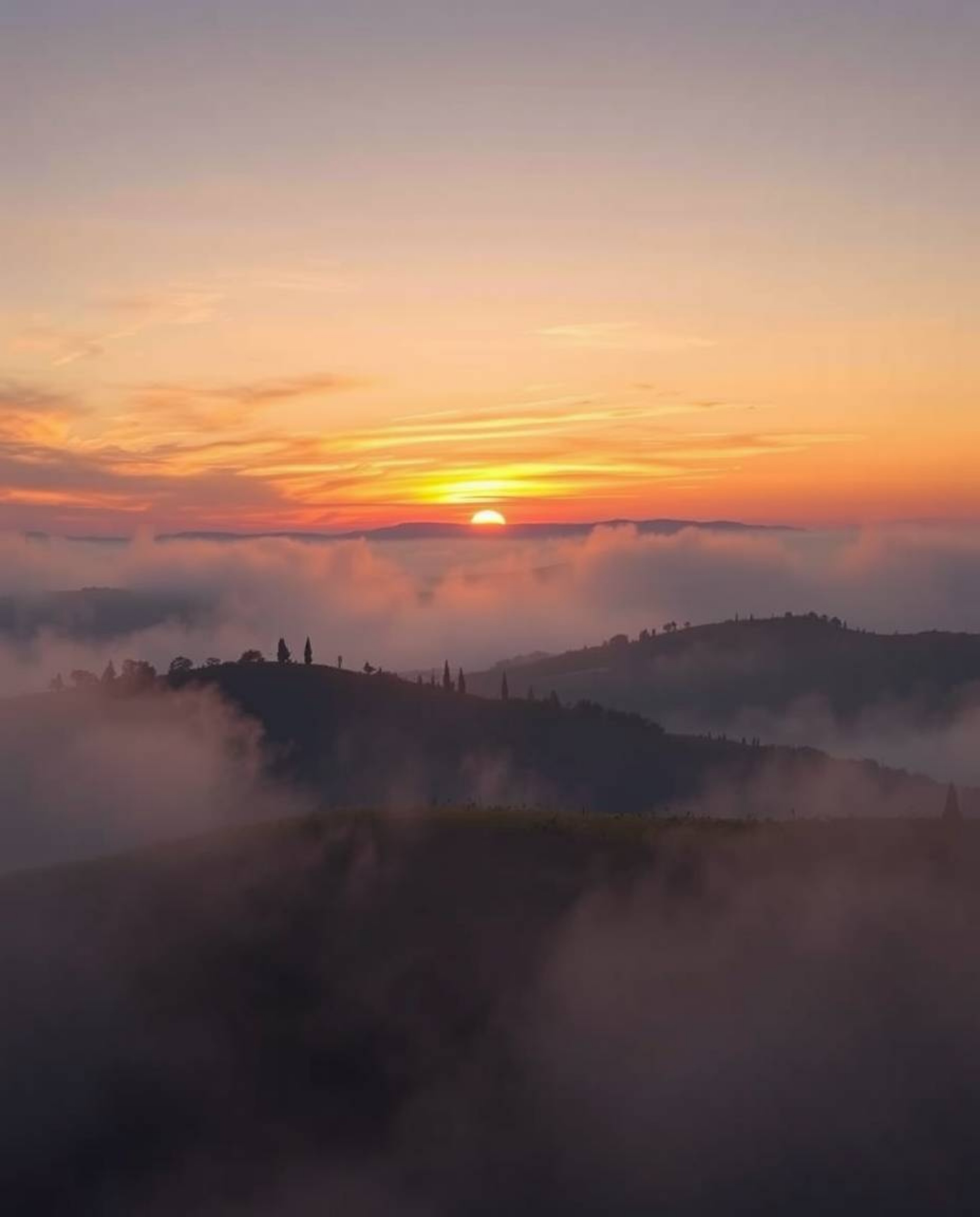 This image captures a breathtaking sunset over misty Tuscan hills, distinguished by its use of volumetric lighting and vibran