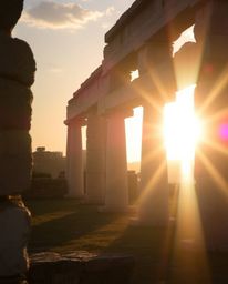 A bright lens flare with soft pastel colors depicts a sunset casting shadows through ancient stone ruins. This gentle and soo