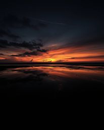 A dramatic chiaroscuro image depicts a sunset sky mirrored in the tidal pools of a beach. This powerful composition is define