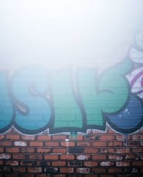 High-resolution stock photo depicting vibrant graffiti-style splashes in blues, greens, and purples on a brick wall, shrouded