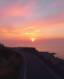 This is a soft pastel painting of a sunset sky over a winding coastal highway. The artwork is characterized by a beautiful bl