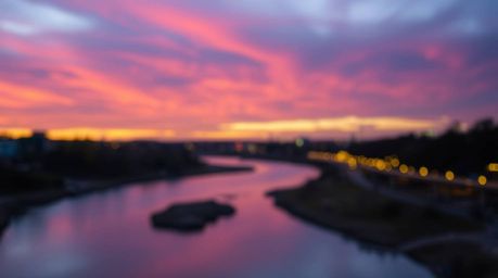 Capture the essence of a winding river reflecting a dramatic orange-pink sunset sky, enhanced with a soft bokeh effect. This 