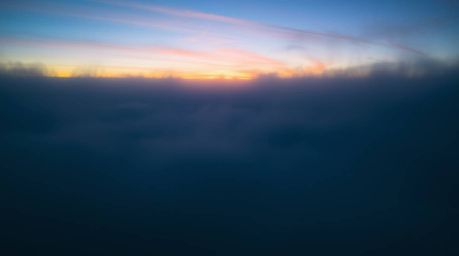 Witness a breathtaking spectacle of nature as the Northern Lights emerge from a thick fog-shrouded sunset sky.  Blues, greens