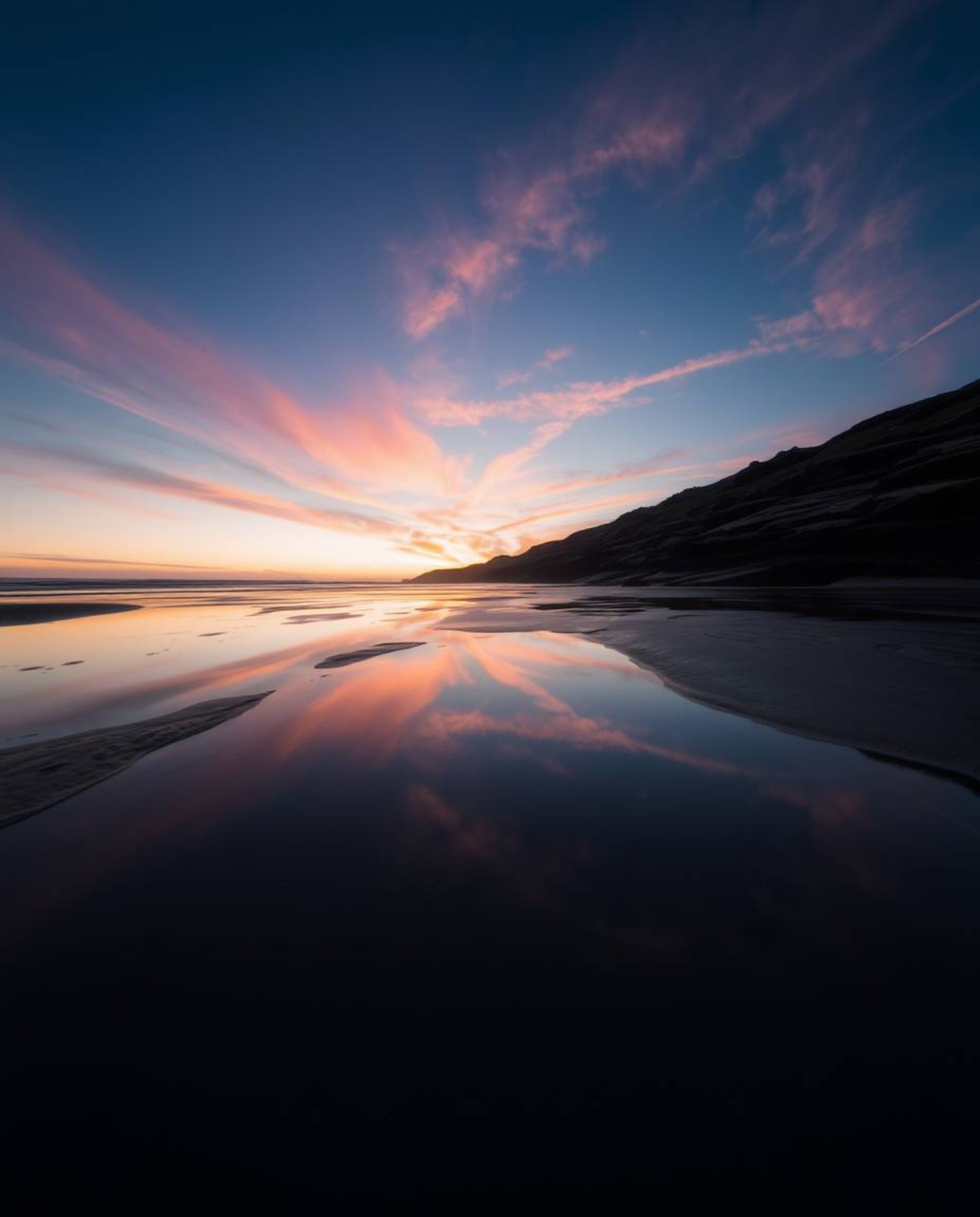 This is a high-angle, long exposure photograph of a sunset sky mirrored in tidal pools on the beach. Taken from an elevated p